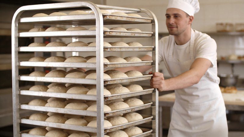 A baker easily pushing a lightweight aluminum trolley full of dough trays